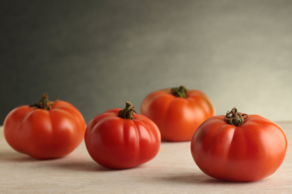 Four shiny Beefsteak Tomatoes on a wooden table.