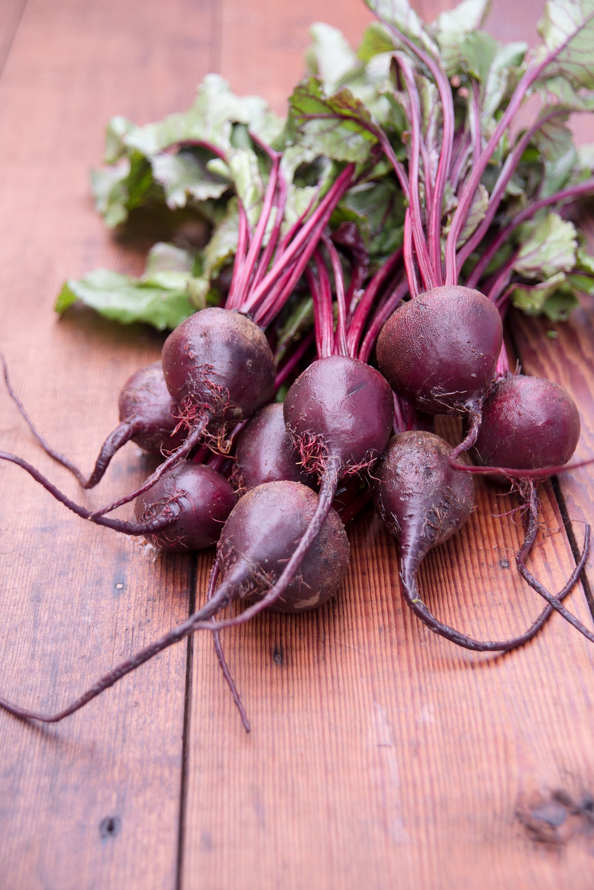 Harvest of fresh beets with greens on a rustic wooden table.