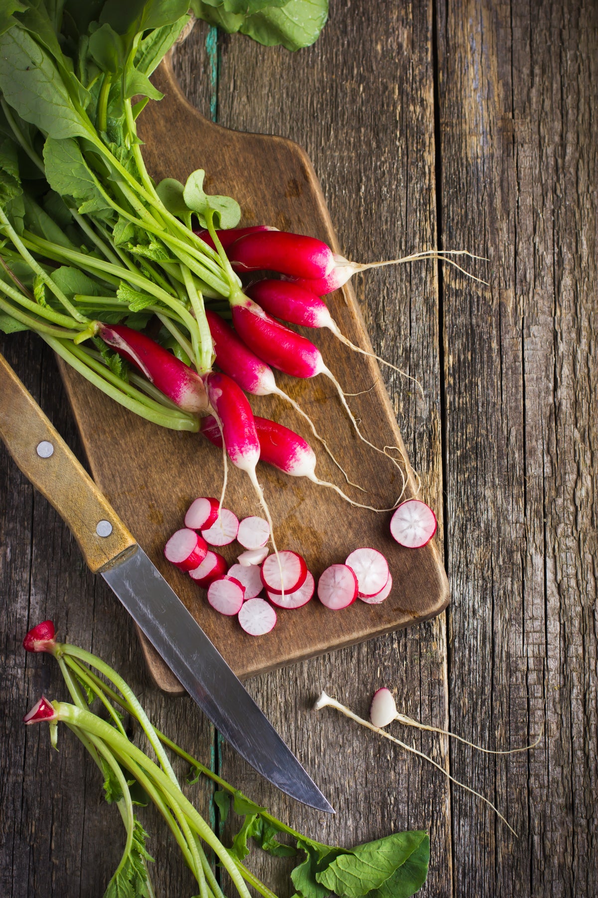 French Breakfast Radish with greens on a cutting board on a rustic wooden table.