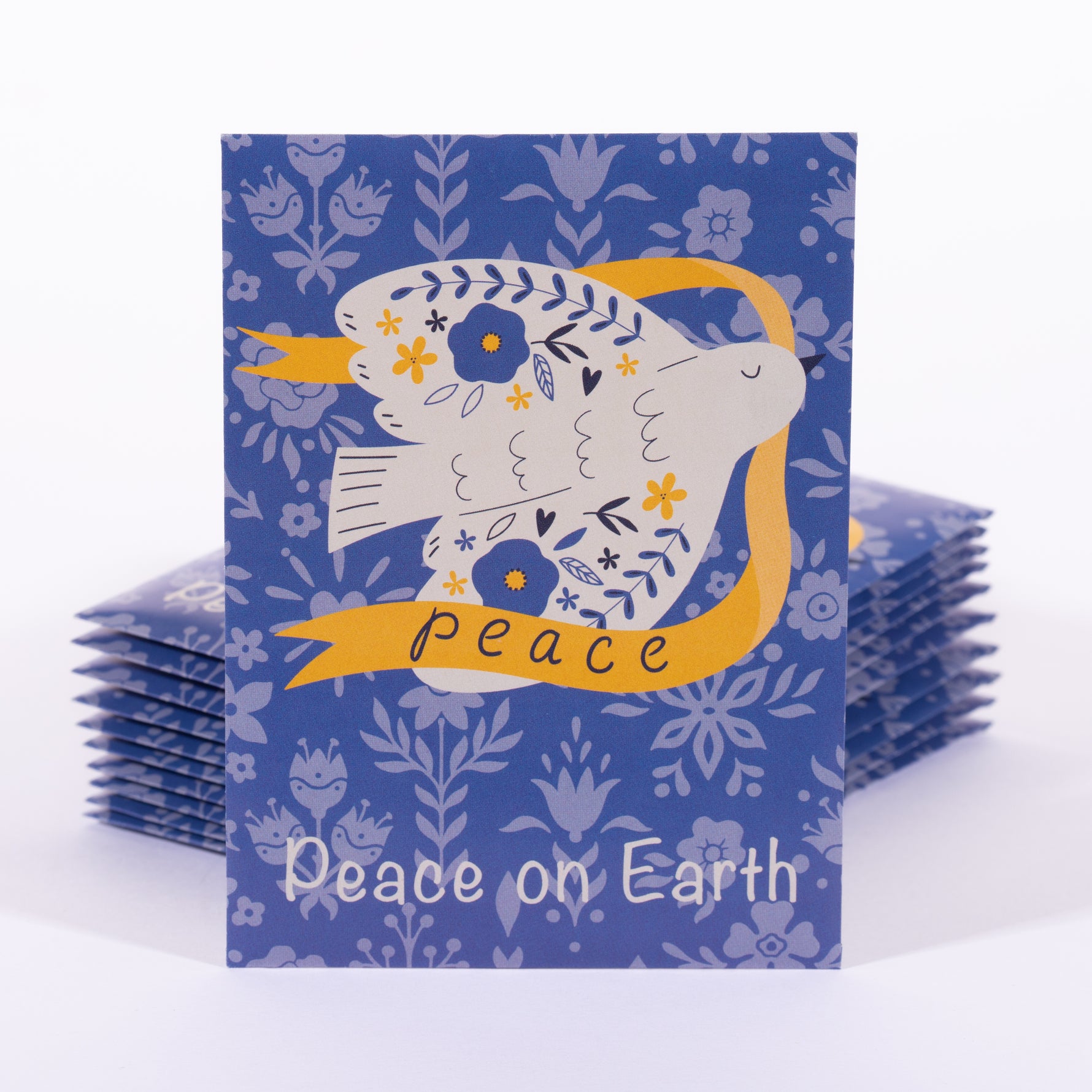 Stack of greeting card seed packets with a peace dove illustration and 'Peace on Earth' text on a blue floral patterned background.