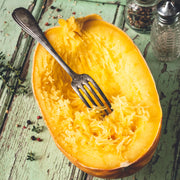 Image of Spaghetti Squash, cut in half with a fork in the center, laying on a rustic wooden table painted light green.