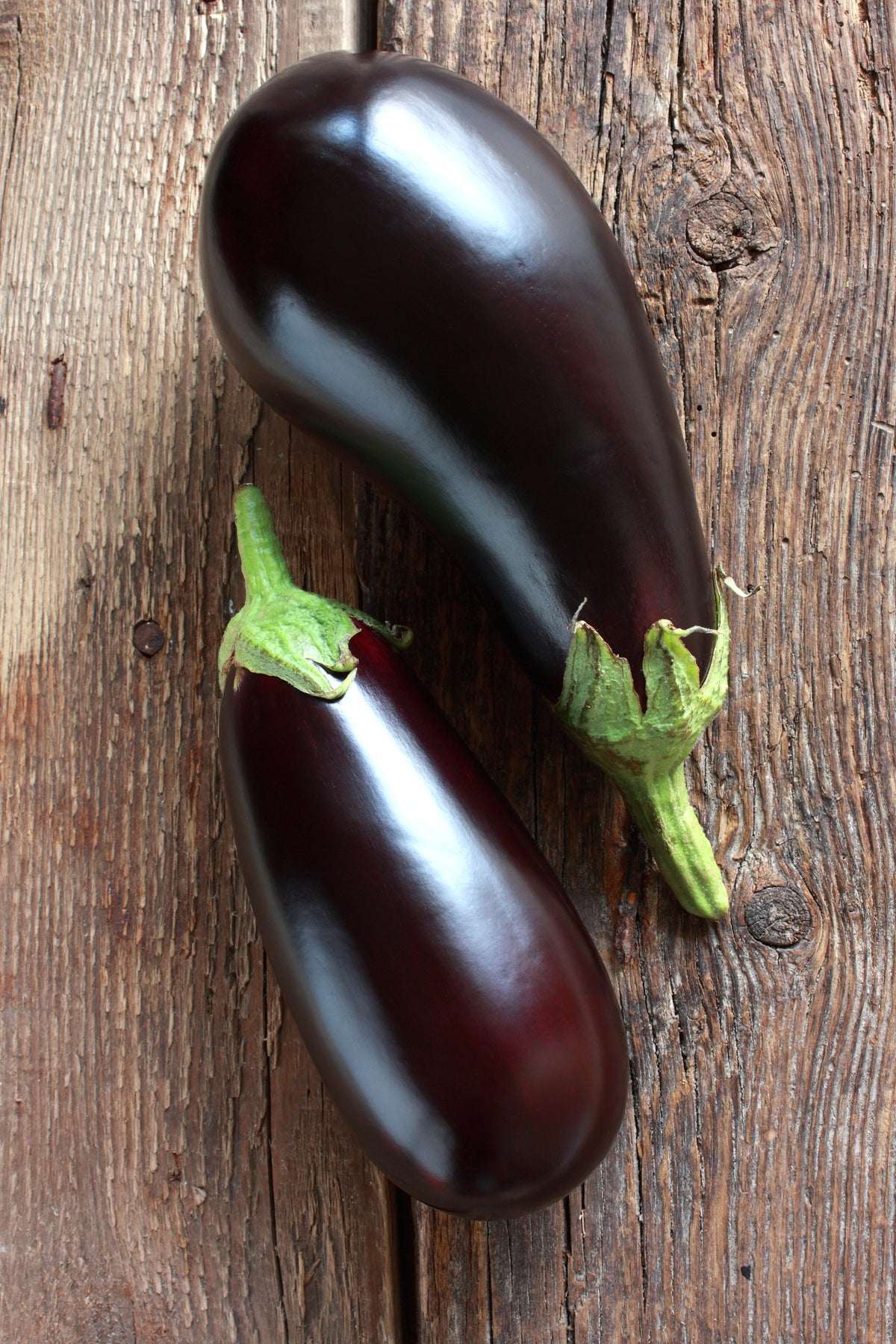 Two eggplants on rustic wooden table.