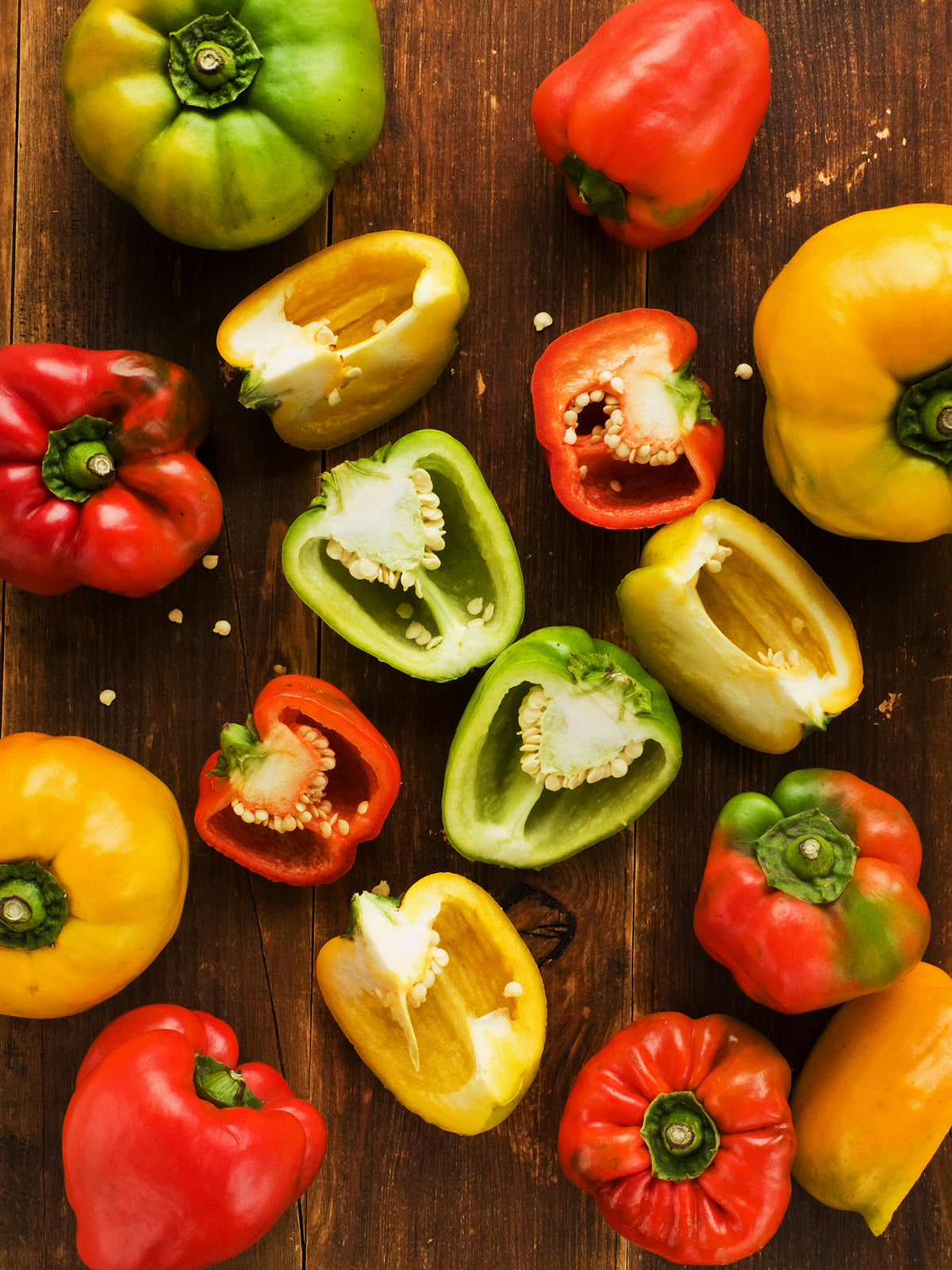 A collection of sliced red, yellow and green peppers on a rustic wooden table. 