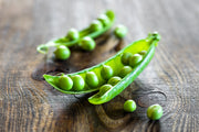 Fresh green peas in a pod on a rustic wooden table.