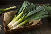 Fresh leeks in a basket on a rustic wooden table.